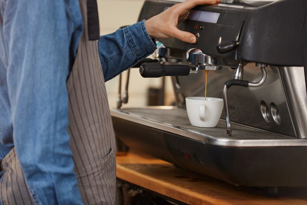 A person operates a coffee maker machine for business, expertly brewing coffee into a white cup placed under the portafilter to elevate office coffee culture.